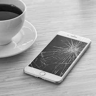 Un téléphone à l'écran cassé et une tasse de café sur la gauche